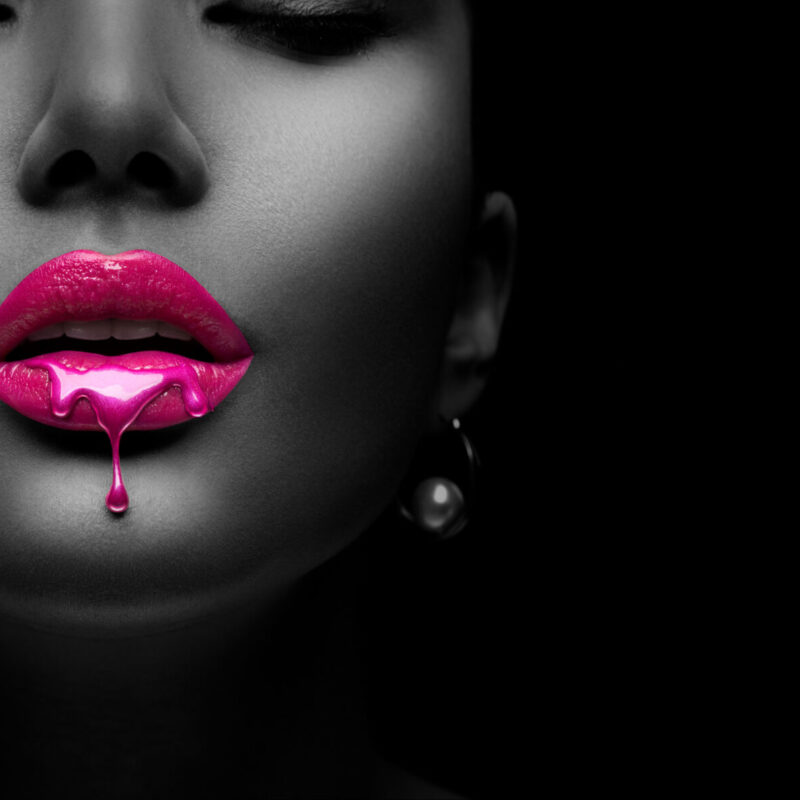 Purple Paint dripping, lipgloss drops on sexy lips, bright liquid paint on beautiful model girl's mouth. Lipstick. Make-up. Beauty face makeup, close up. Isolated on black background